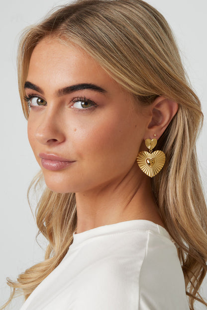Close-up of a woman wearing gold heart-shaped drop earrings with a soft, youthful look