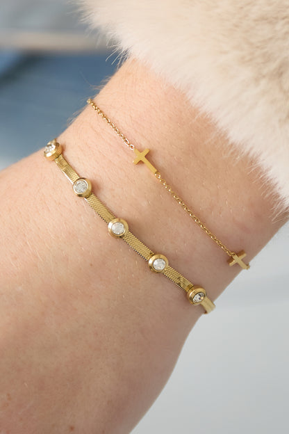 Close-up image of a woman’s wrist wearing the gold cross chain bracelet paired with a gold rhinestone bracelet.