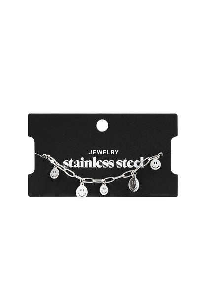 Silver stainless steel chain bracelet featuring four small dangling happy face charms on a black display card.