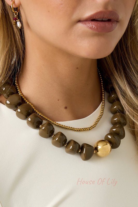 Close-up of the chunky brown beaded necklace layered with a gold bead chain on a woman wearing white top