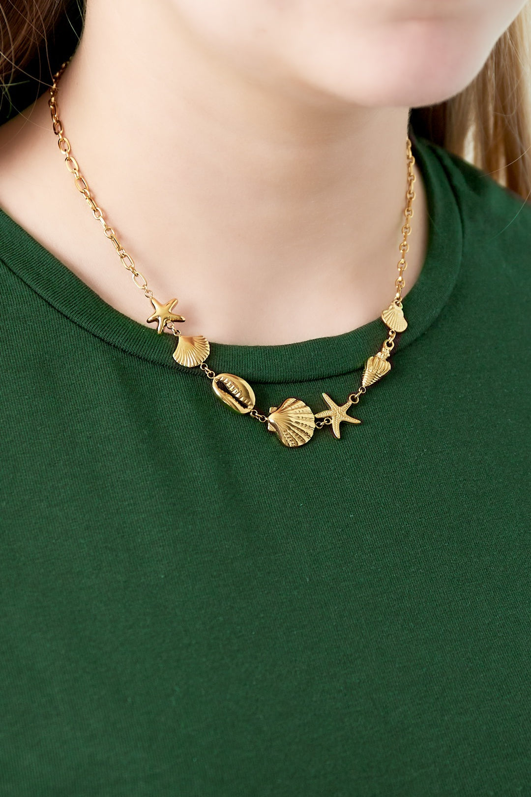 Close-up of gold seaside charm necklace being worn on woman with green top highlighting starfish and shell charms