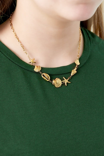 Close-up of gold seaside charm necklace being worn on woman with green top highlighting starfish and shell charms