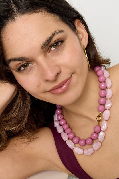 Woman wearing layered pink and light pink chunky beaded necklaces with gold hoop earrings and maroon tank top