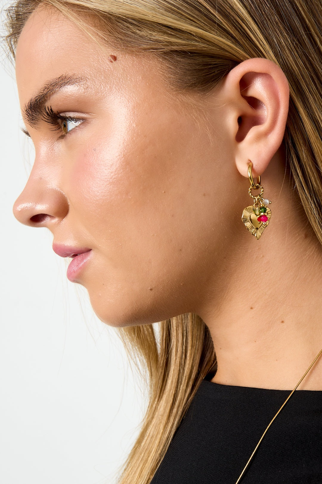 Close-up of model wearing one gold-tone heart charm earring with pink and green beads and pearl accent