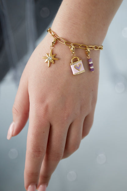 Close-up of a woman's wrist wearing the gold charm bracelet with pastel lilac and crystal charms against a soft-focus background