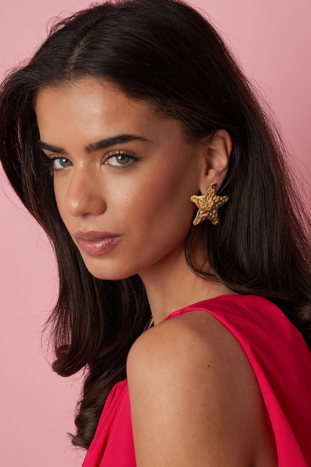 Model wearing gold textured starfish stud earrings with pink background and red outfit