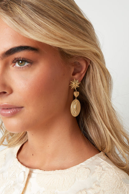 Close-up of a woman wearing the gold sun and heart dangle earring, showcasing its elegant design and how it complements her outfit.