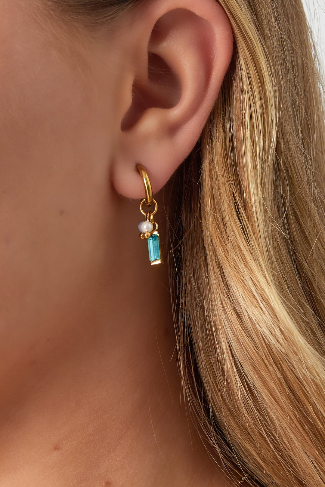 Gold hoop earring with aqua rectangular gemstone, pearl, and small bead displayed on woman's ear with blonde hair