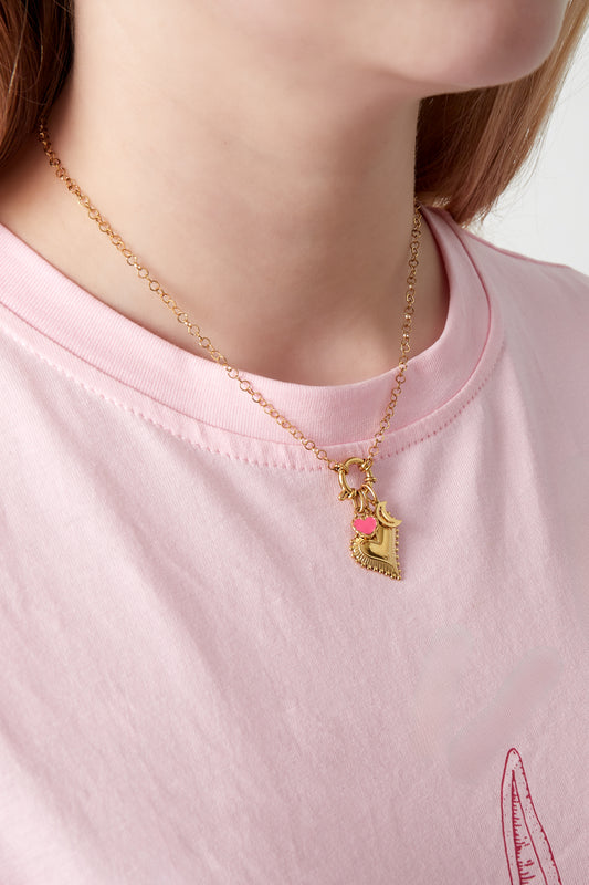 Close-up of a woman wearing the gold charm necklace over a pink t-shirt, displaying the heart and other charms clustered near the neckline