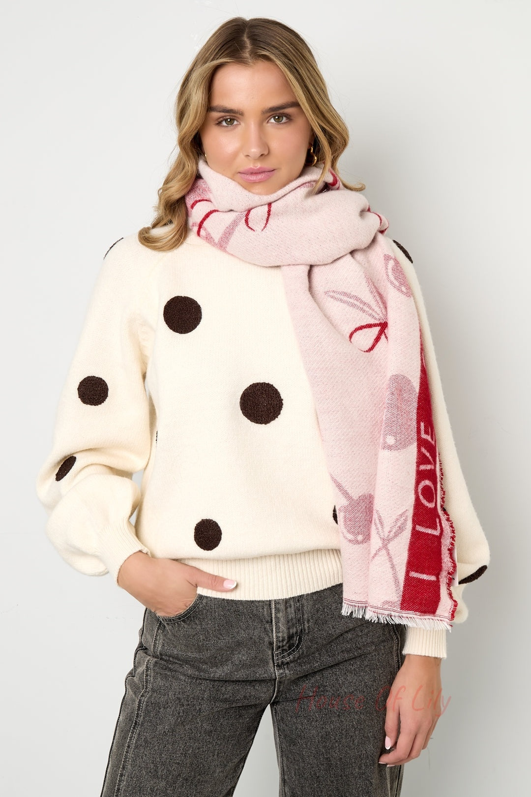 Woman wearing a light pink and red cherry print scarf styled over polka dot sweater and black jeans