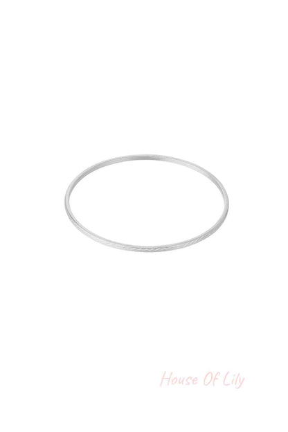 Single slim silver bangle with a delicate engraved pattern on white background