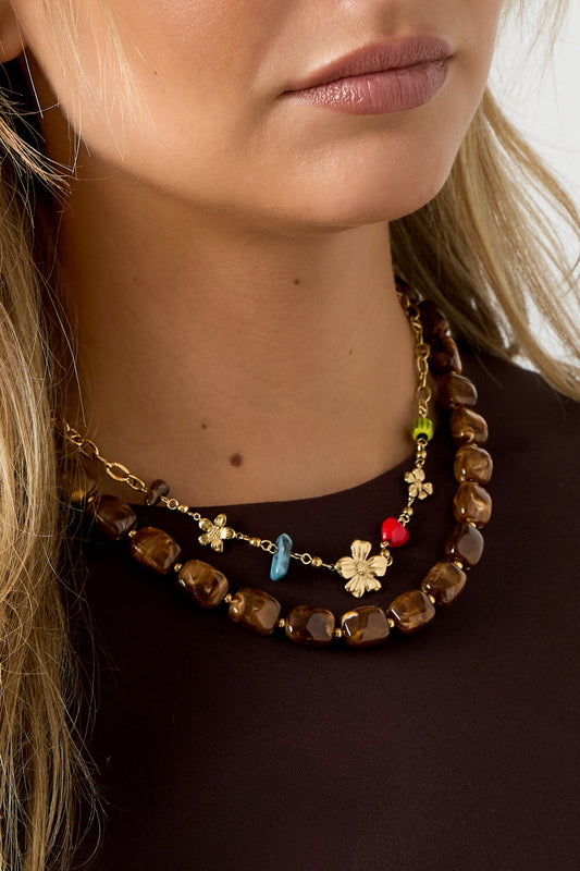 Close-up of model wearing the gold flower charm necklace layered with a chunky brown necklace
