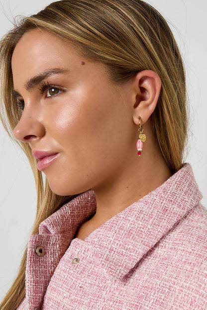 Close-up side profile of a woman wearing a gold hoop earring with pink bead and gold heart charm, styled with a pink textured jacket