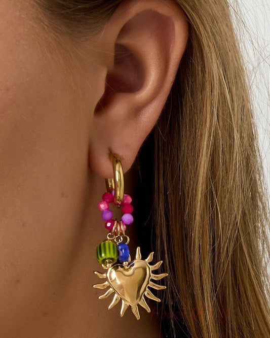 Side view close-up of a woman’s ear wearing a gold sunburst heart hoop earring with vibrant pink and green beads
