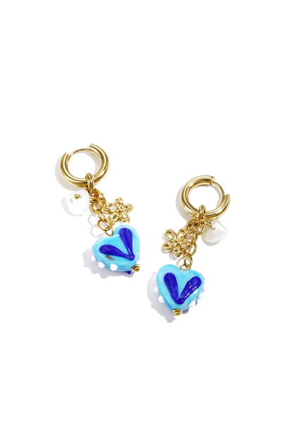 Gold hoop earrings with dangling blue heart charms decorated with dark blue and white details and small gold flower charms on white background