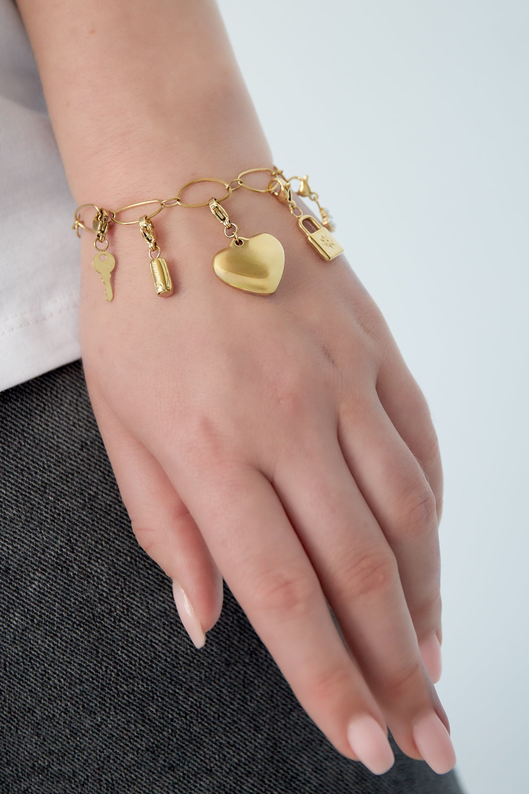 Woman wearing the golden charm link bracelet on wrist showcasing dangling charms including heart and key