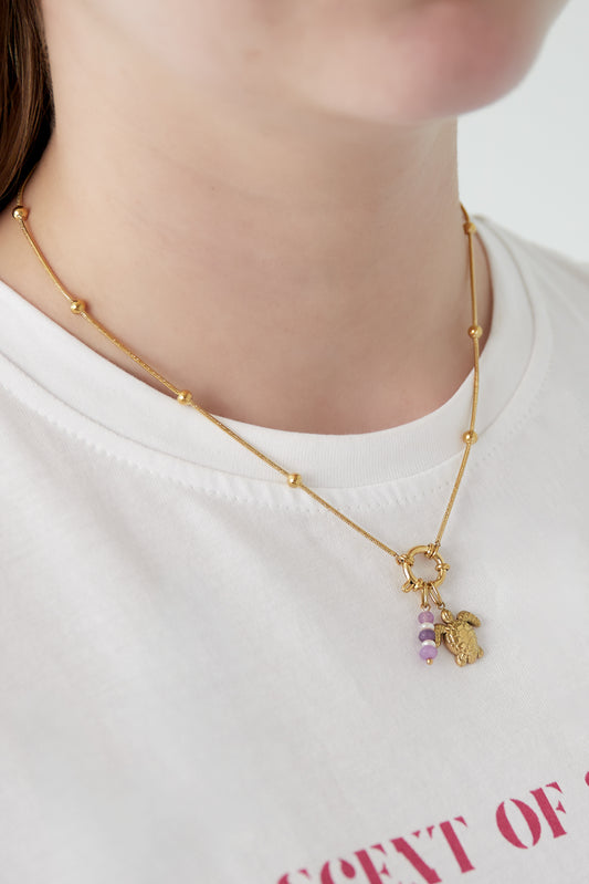 Close-up of woman wearing the gold charm necklace featuring turtle and purple bead charms against a white shirt