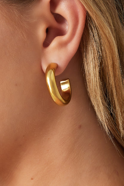 Close-up of a woman wearing chunky gold-tone hoop earring showcasing thick smooth design