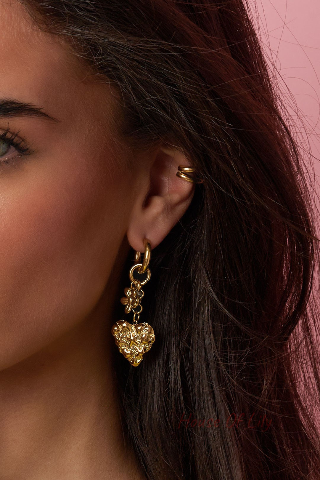 Close-up of model’s ear showcasing detailed gold heart drop earring with floral and pearl accents