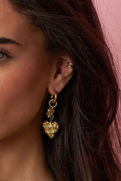 Close-up of model’s ear showcasing detailed gold heart drop earring with floral and pearl accents