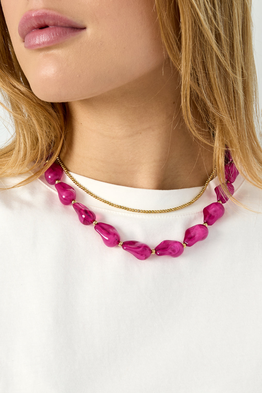 Side angle close-up of pink acrylic beaded necklace showcased on woman wearing white shirt