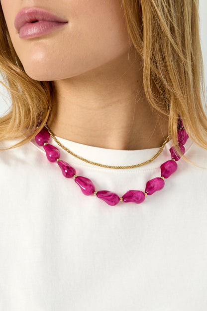 Side angle close-up of pink acrylic beaded necklace showcased on woman wearing white shirt
