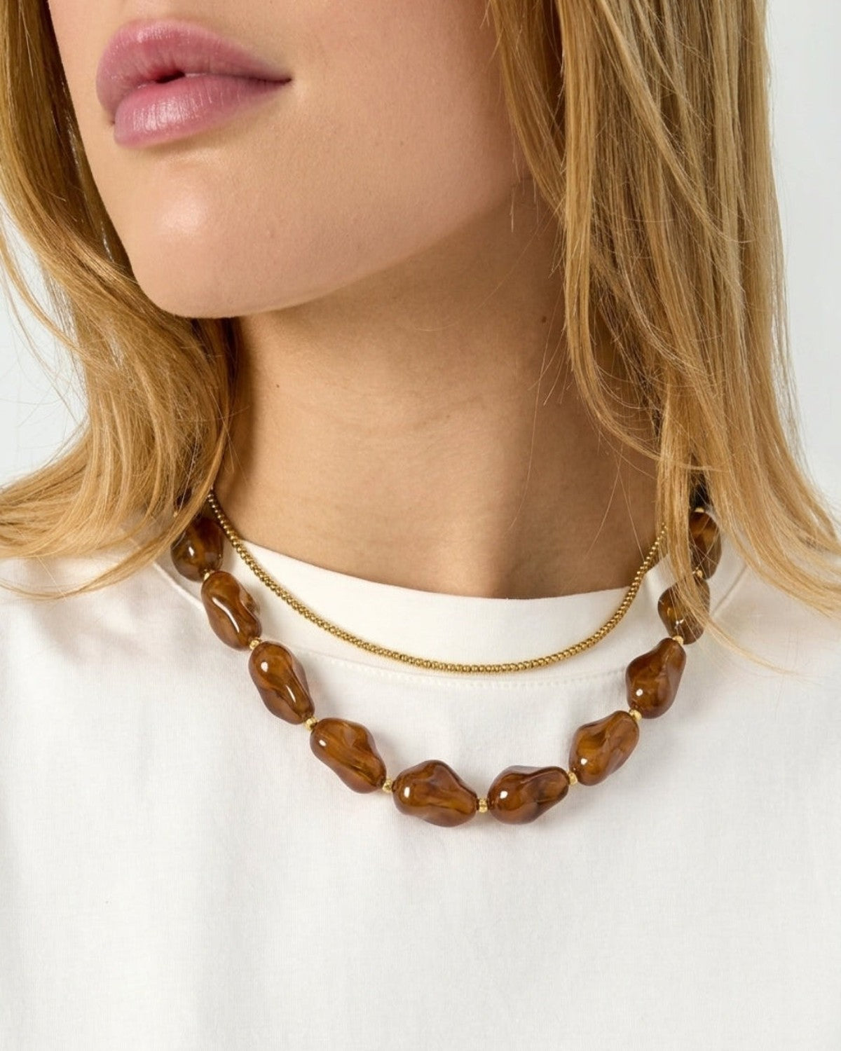 A woman wearing a chunky marbled brown beaded necklace paired with a delicate gold chain necklace.