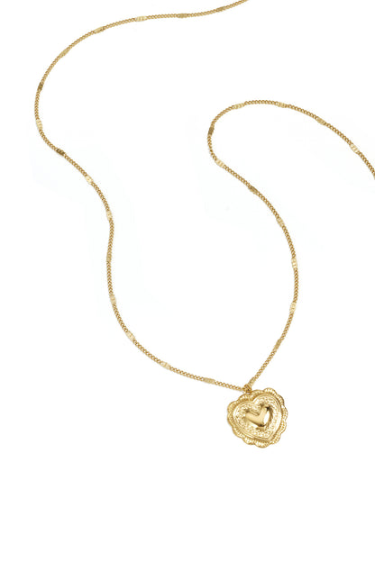Close-up of gold long necklace with heart-shaped embossed pendant on white background