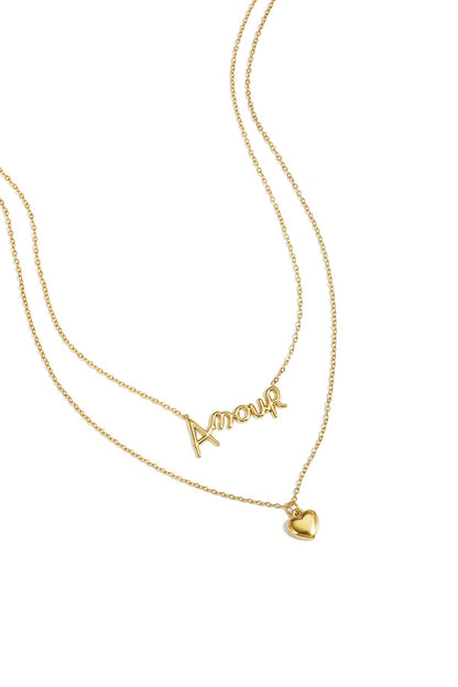 Close-up of gold layered necklace with ‘Amour’ script and heart pendant on white background