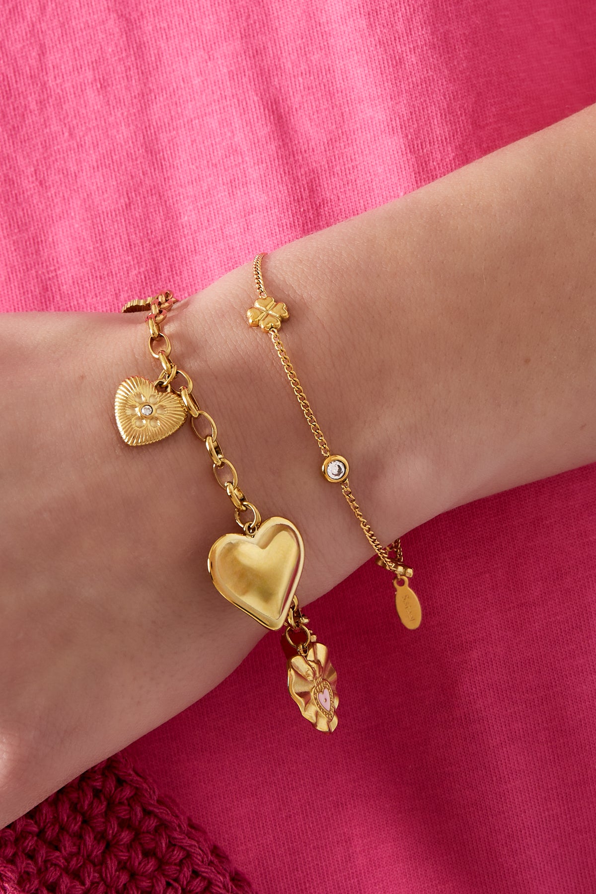 Close-up of a wrist wearing two gold bracelets including the delicate four-leaf clover charm bracelet, styled with pink clothing