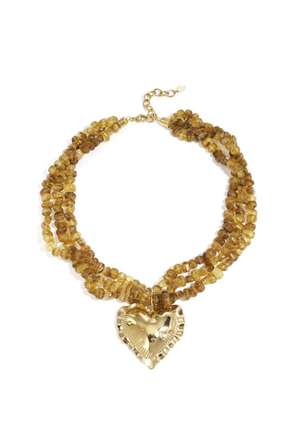 Close-up of twisted amber-colored beaded necklace with a large shiny gold heart pendant on white background