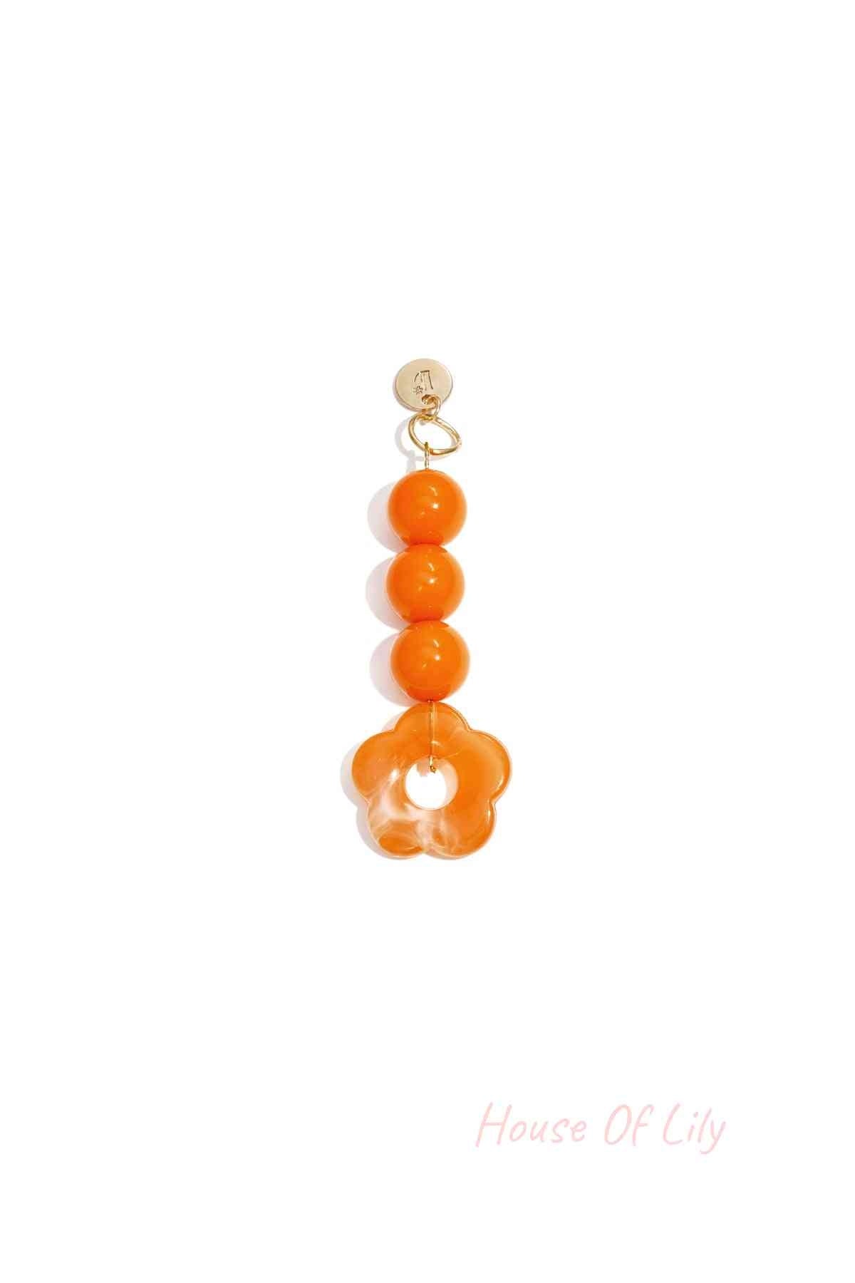 Orange acrylic flower bag charm with three round orange beads hanging from a gold clasp on white background