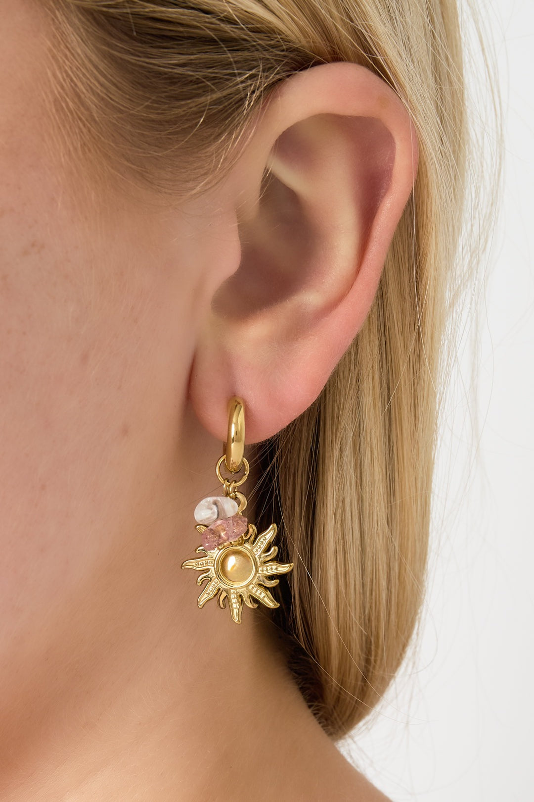 Close-up of a woman's ear wearing a gold sun charm drop earring with pink and pearl beads