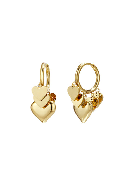 Pair of gold drop earrings with three layered heart charms hanging from hoops on white background