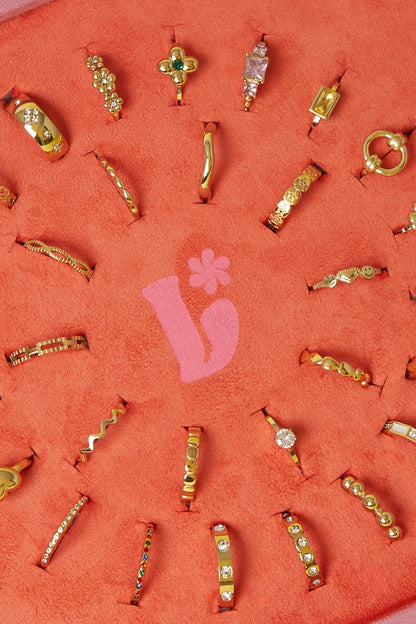 Close-up detail of gold-tone rings on coral-orange velvet display featuring rhinestones, floral and heart shapes