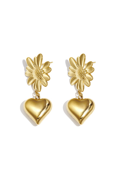 Pair of gold drop earrings featuring a textured flower base and a hanging shiny heart pendant on white background