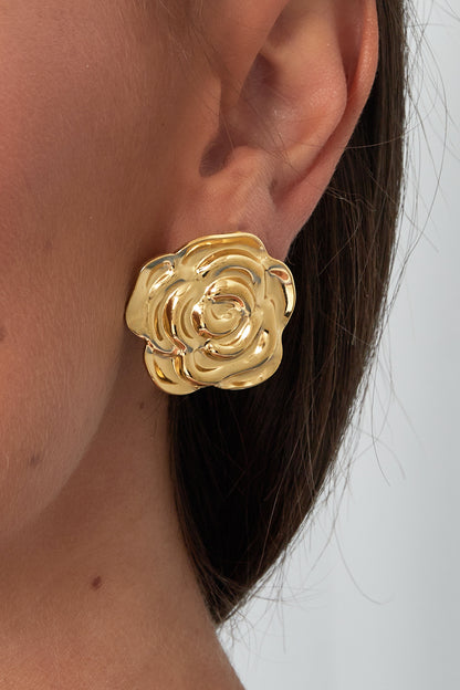 Close-up of a woman wearing a single gold floral stud earring highlighting its polished textured rose design