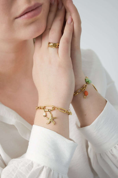 Gold starfish bracelet worn on wrist with white long sleeve shirt, close-up of hand and bracelet