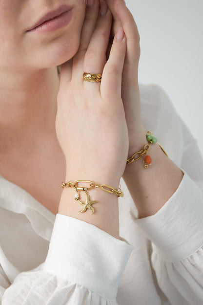 Gold starfish bracelet worn on wrist with white long sleeve shirt, close-up of hand and bracelet