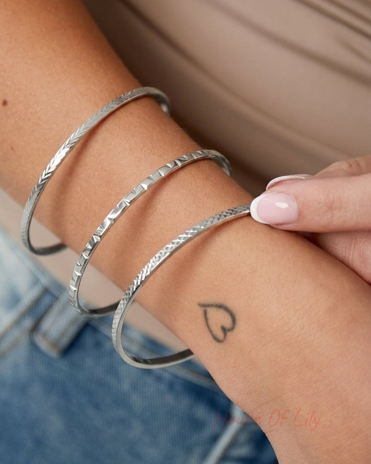 Three slim gold-toned metal bangles featuring distinct geometric textures worn on a wrist.