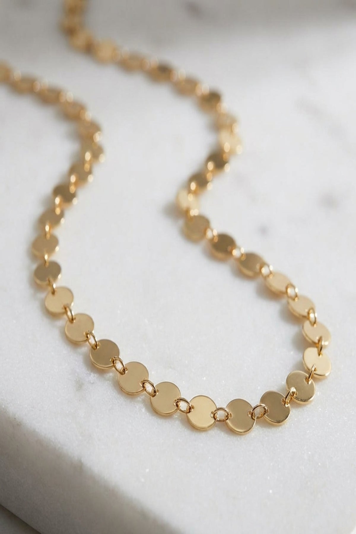 Close-up of Dainty Disc Chain Necklace with reflective discs on textured white marble, showcasing fine links and polished stainless steel finish.