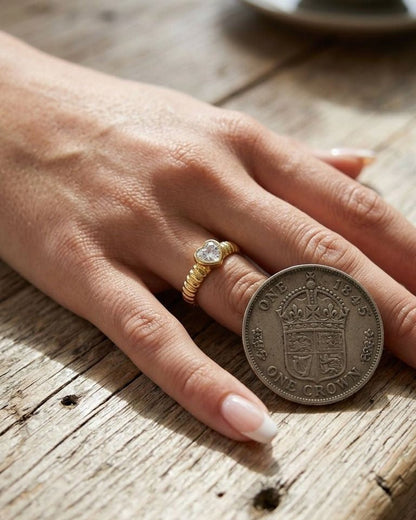 Delicate heart-shaped ring in polished gold-tone stainless steel resting on textured wooden surface, highlighting its elegance and craftsmanship.