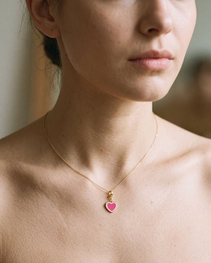 Dainty heart-shaped enamel pendant on a delicate gold chain necklace worn around the neck.