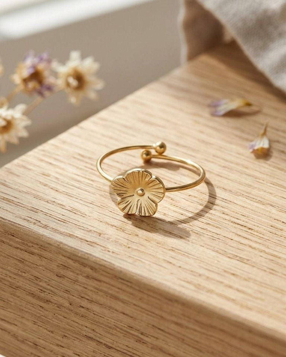 Close-up of Daisy Flex Gold ring with sculpted flower detail on wooden surface in natural light