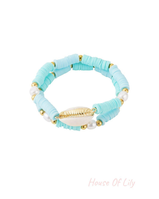 Light blue shell beaded bracelet set composed of polymer bead discs, faux pearls, and gold-tone shell charm on white background