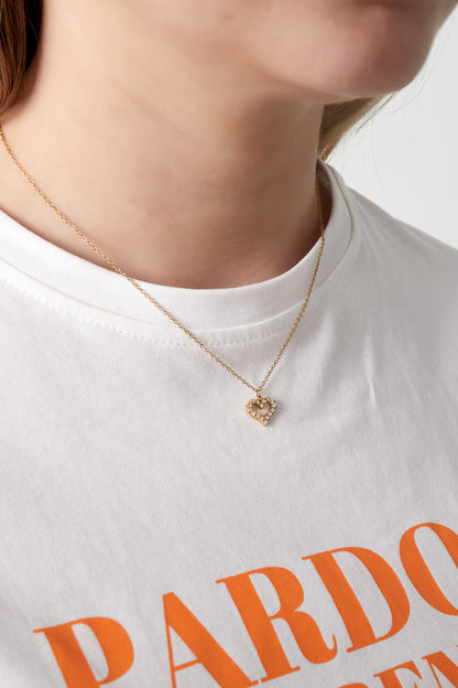 Close-up of woman wearing gold rhinestone heart pendant necklace with white printed t-shirt