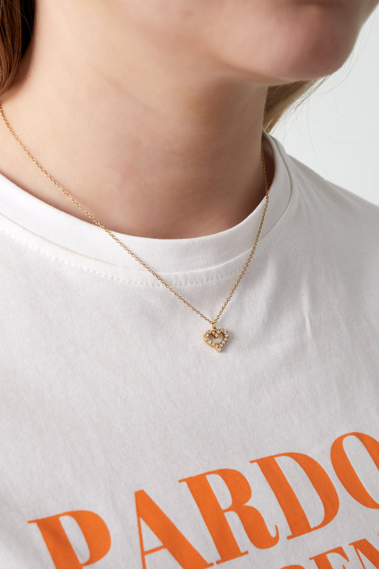 Close-up of woman wearing gold rhinestone heart pendant necklace with white printed t-shirt
