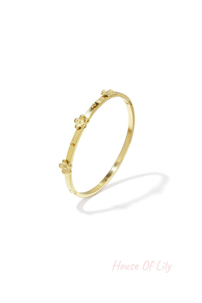 Gold-toned slim metal bangle bracelet featuring small raised floral decorations, shown isolated on white background