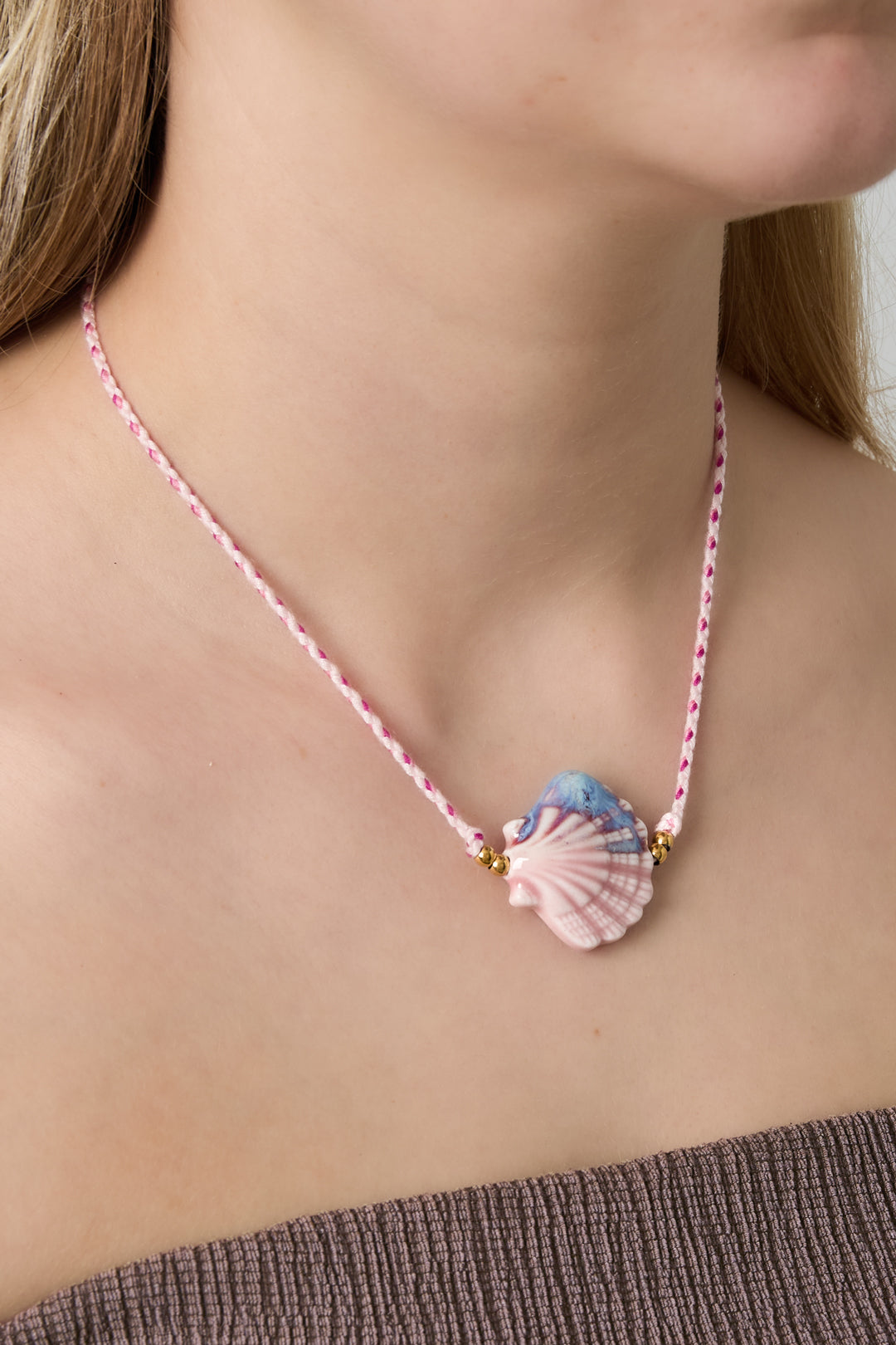 Woman wearing soft pink seashell ceramic pendant necklace on braided pink cord