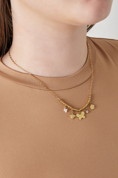 Model wearing the gold charm beaded necklace with butterfly, bee and floral charms on a brown top